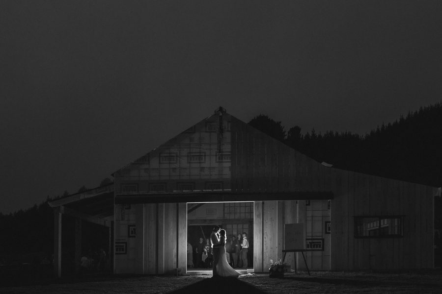 Bride and groom kissing in the barn at night with guests watching