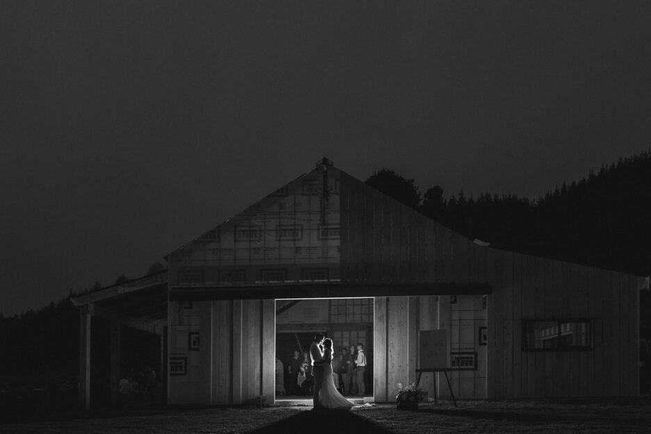 Bride and groom kissing in the barn at night with guests watching