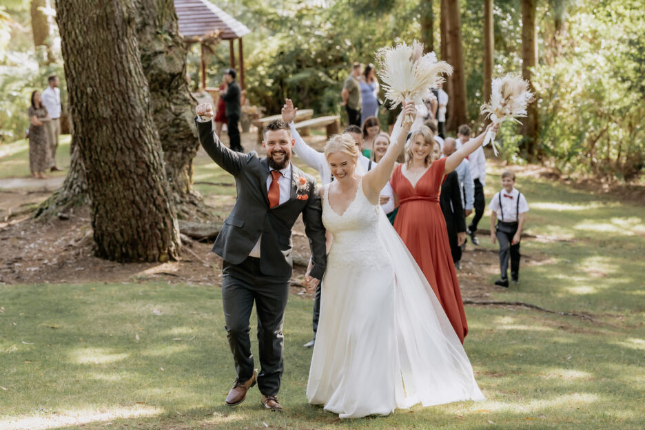 Happy bridal party walk down aisle holding up hands