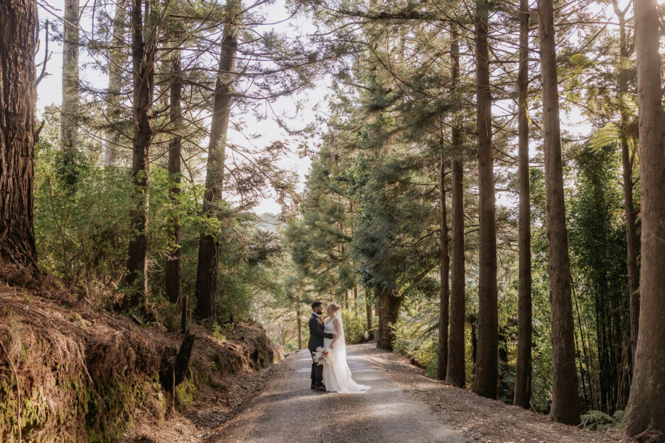 Bride and groom in driveway under redwoods at Falls Retreat Waihi