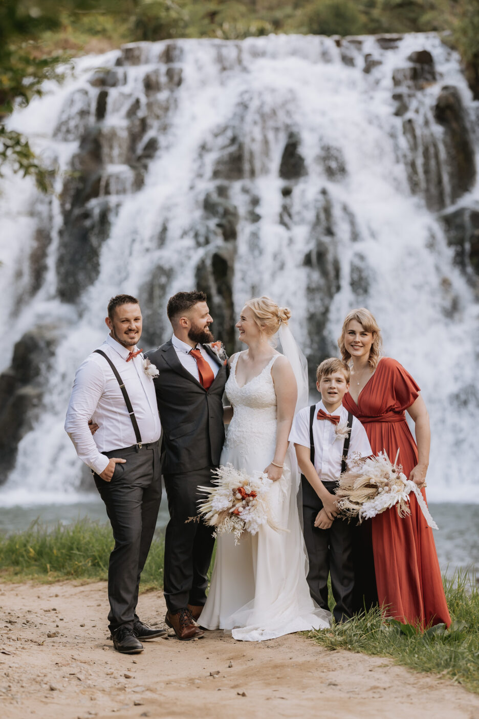 Wedding party stands in front of Owharoa Falls in Karangahake Gorge