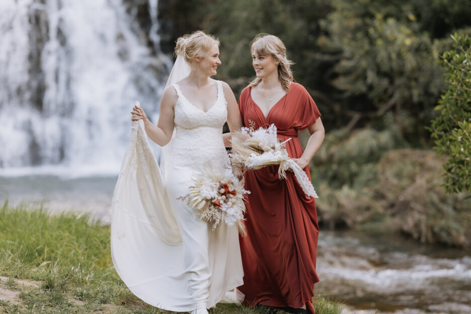 Bride and bridesmaid walking in front of waterfalls at Falls Retreat Waihi