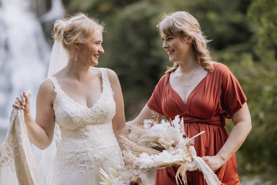 Bride with her bridesmaid in rust dress by falls at Karangahake Gorge