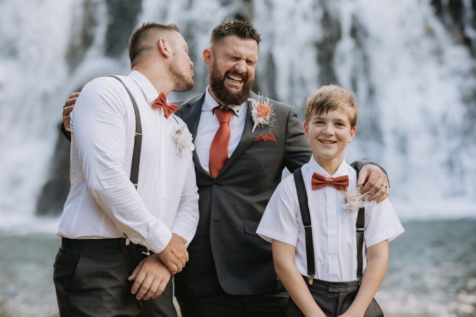 Groomsmen goes to kiss groom by falls at Falls retreat Karangahake Gorge