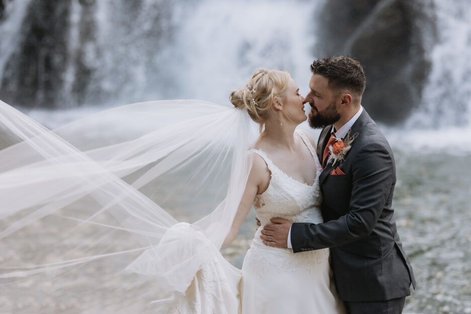 groom kissing bride with veil flying at Karagahake gorge New Zealand