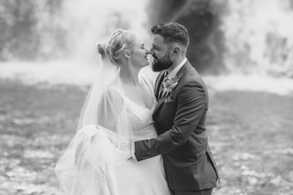 Black and white image of bride and groom at water fall in New Zealand Waihi