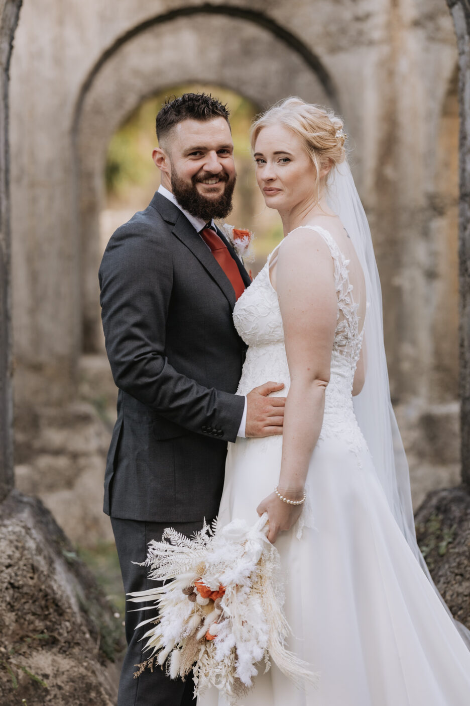 Bride and groom looking at camera in arch of historic place Waihi New Zealand