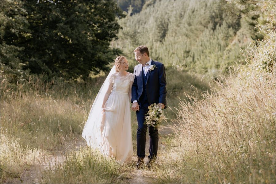 Bridal couple Walking in the Forest wedding photo groom carries flowers