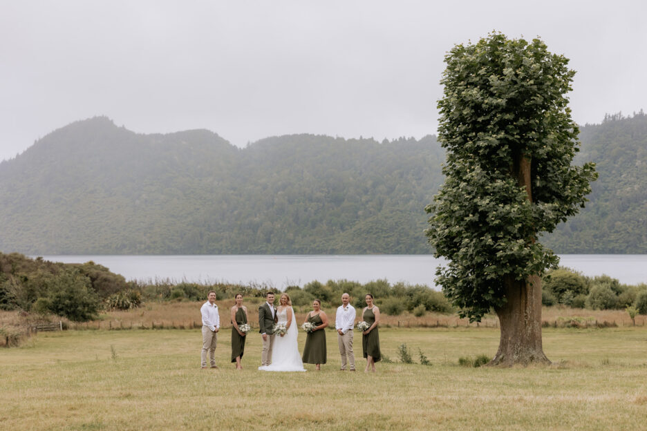 Lake Okareka wedding party in olive green standing by tree in field