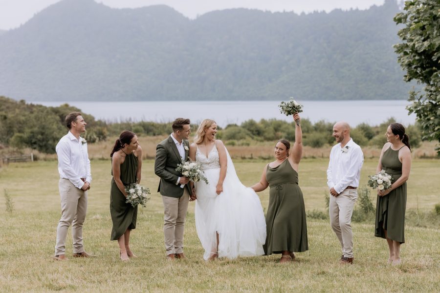 Wedding party walking in front of lake Okareka Rotorua with bridemaid being silly