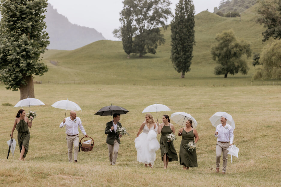 Wedding party walking laughing with umbrellas over field