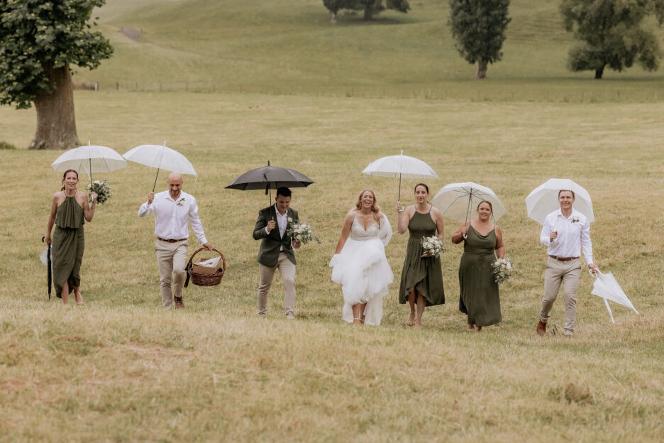 Wedding party walking in the rain with umbrellas at Longfords Estate