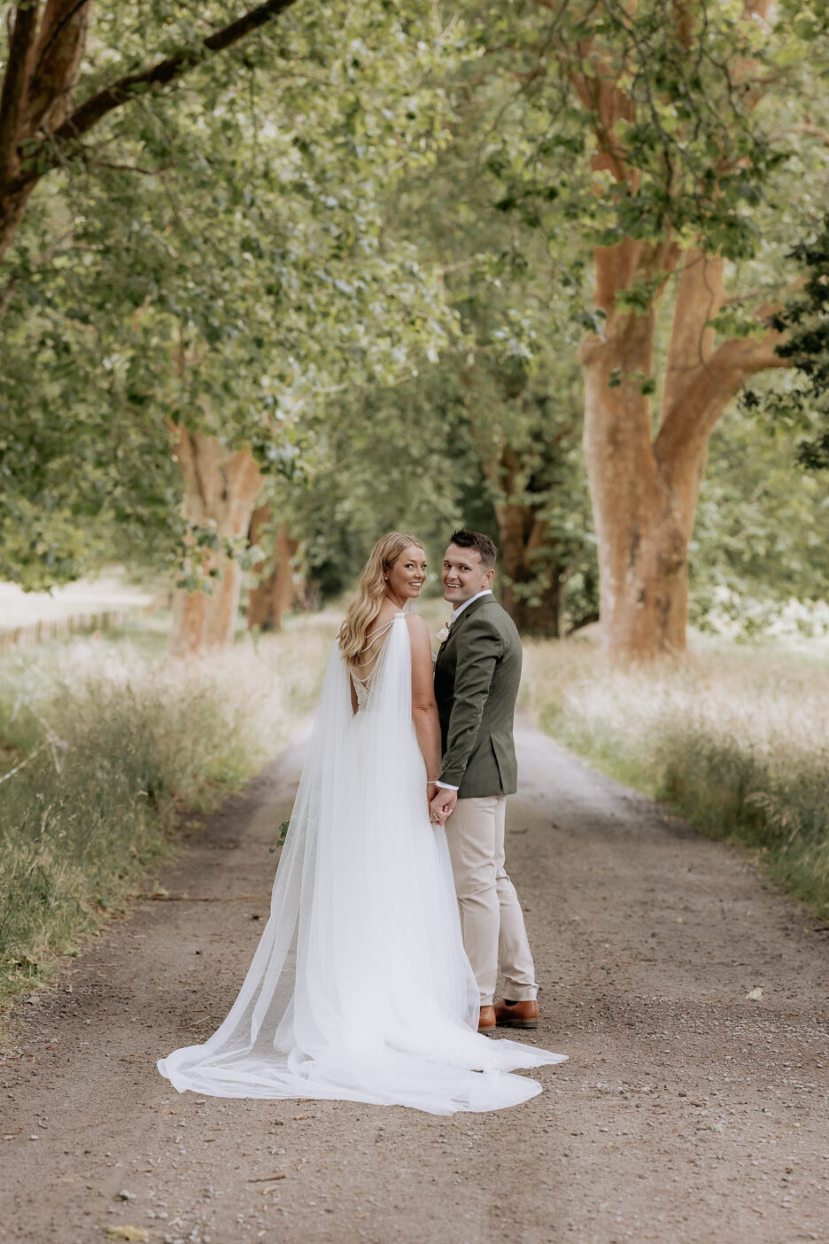 Bride and groom at Longfords estate driveway turning looking at photographer