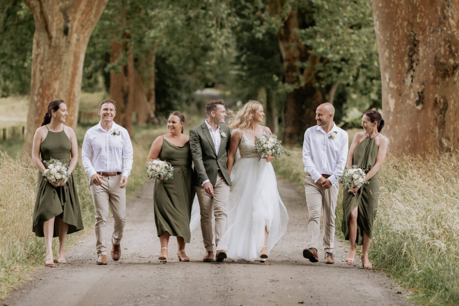 Groom in green jacket with party in country colors walking on driveway smiling laughing