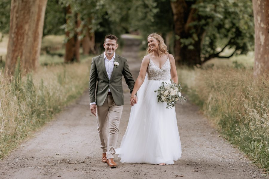 Wedding couple walking laughing together along driveway at longfords Lake Okareka Rotorua