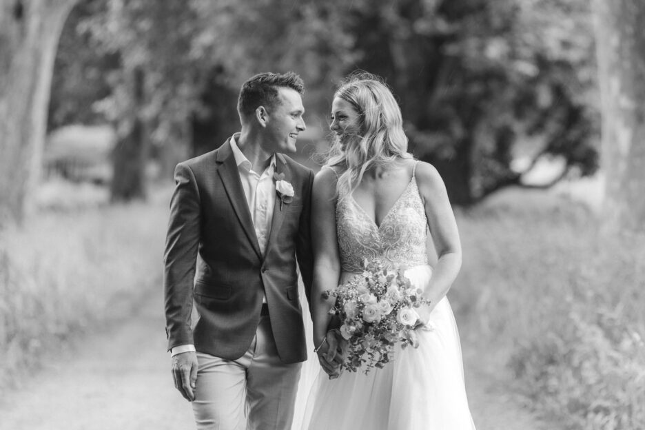 Bride and groom looking at each other while walking on driveway in the rain