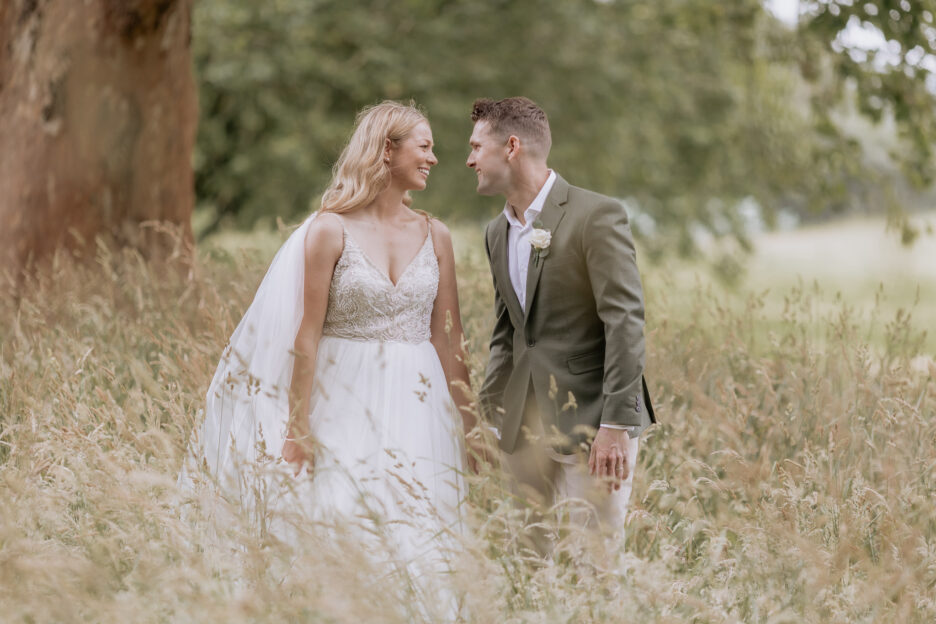 Happy natural image of bride and groom walking in high grass under trees at Longfords Estate