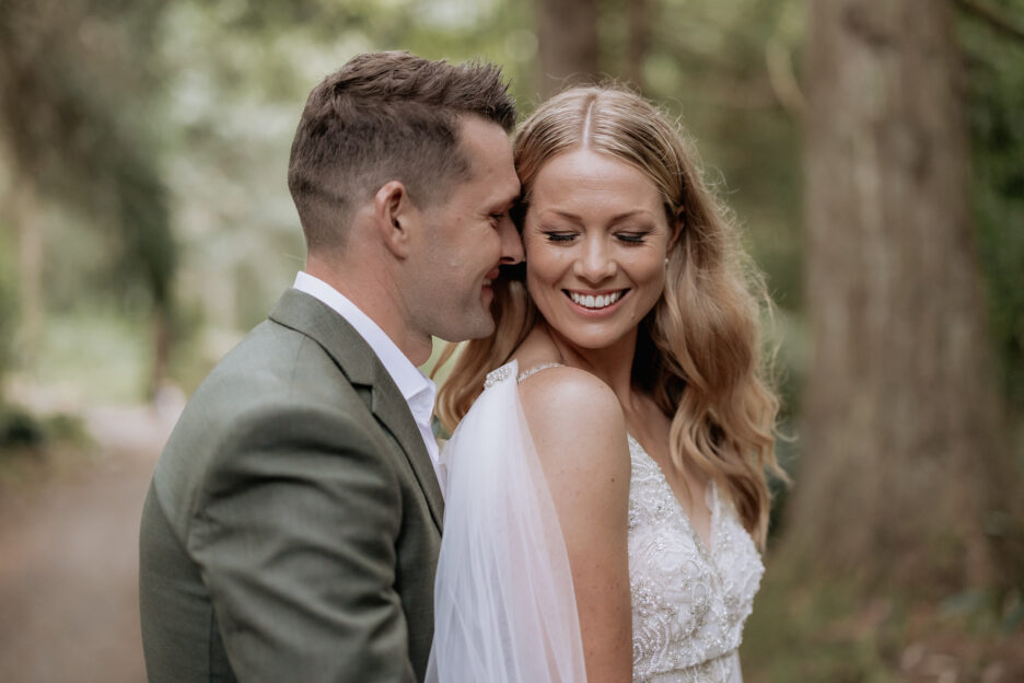 Snuggling bride and groom under redwoods