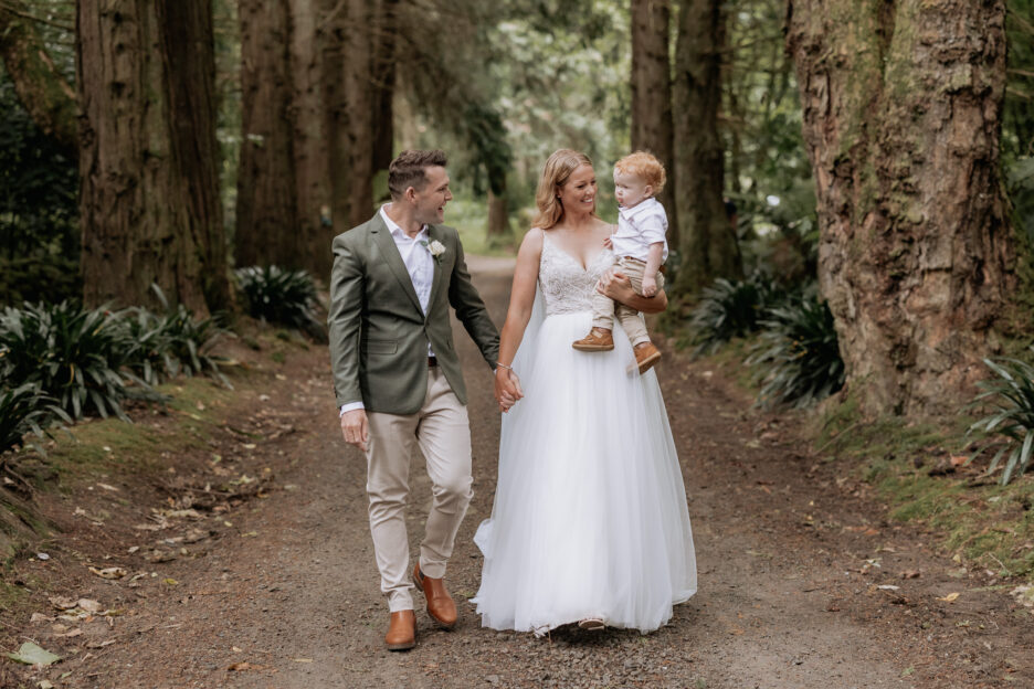 Wedding couple walk with son under the redwoods at Longfords Estate Rotorua