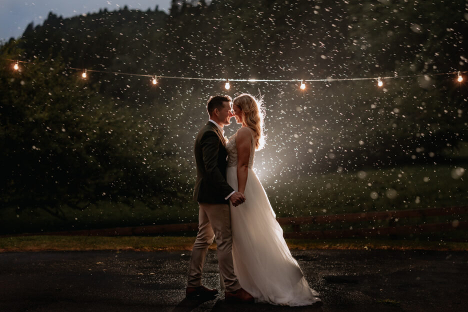 wedding couple stand in the rain as it softly falls around them lit up