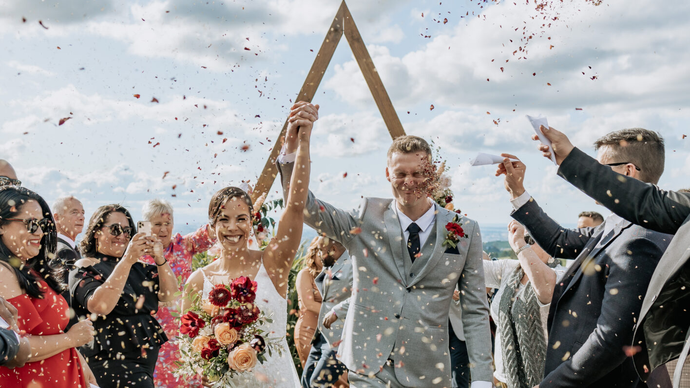 Celebration image of couple happily walking down the aisle with confetti being thrown at groom