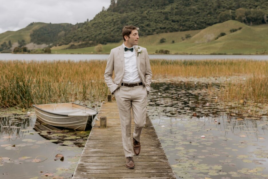 Groom in natural linen suit walks on wharf at lake okareka