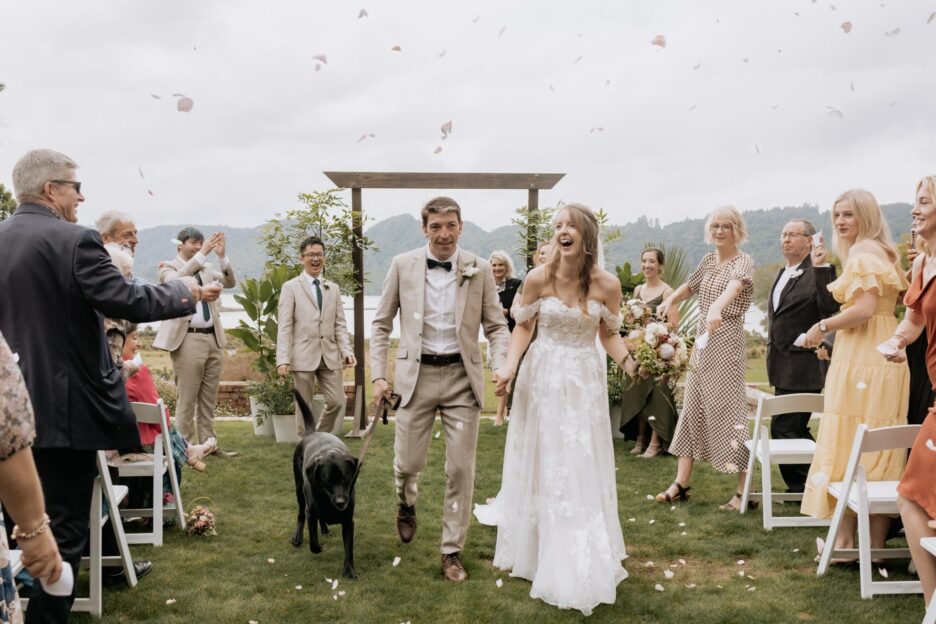 Confetti being thrown as bride and groom and their dog walk aisle