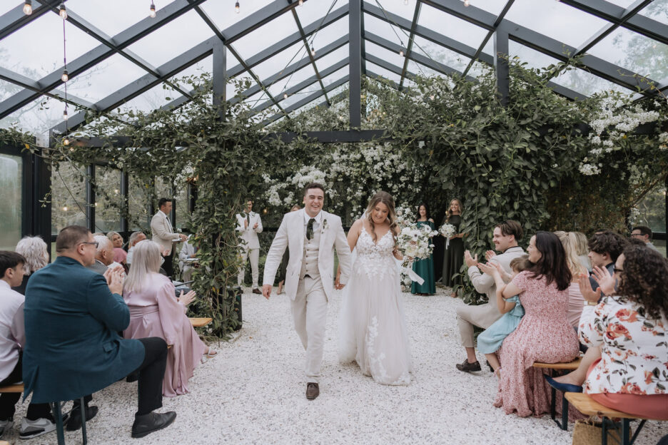 bride and groom walking aisle just married at black walnut glass house