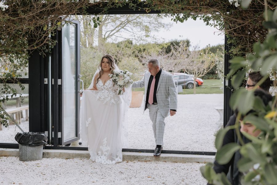 bride walking into black walnut glass house ceremony