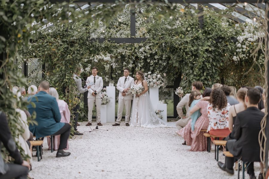 wedding ceremony at black walnut glass house surrounded by green and white