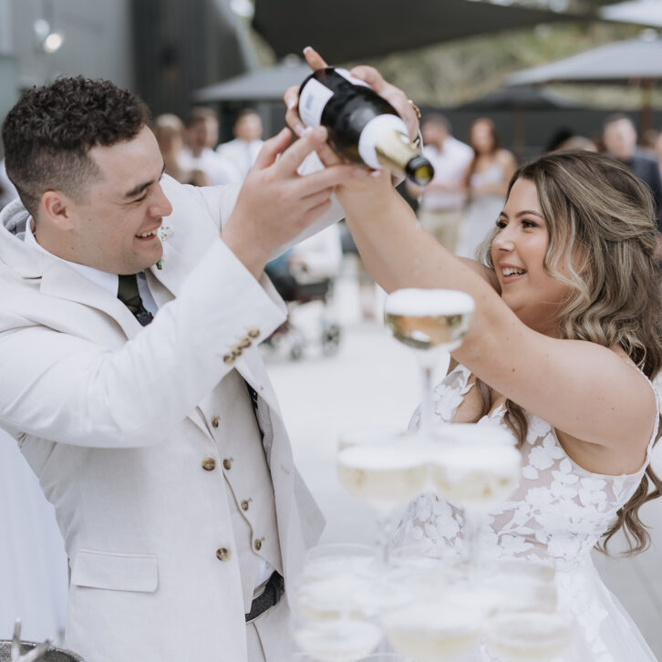 bride and groom filling champagne tower glasses at black walnut wedding venue in Tauranga