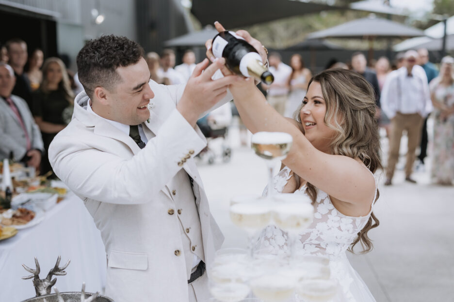 bride and groom filling champagne tower glasses at black walnut wedding venue in Tauranga