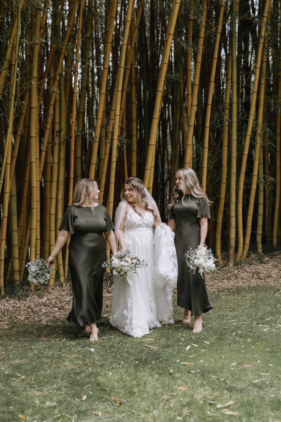 Olive green bridesmaids dresses walking with bride in front of the bamboo trees in olive green black walnut venue