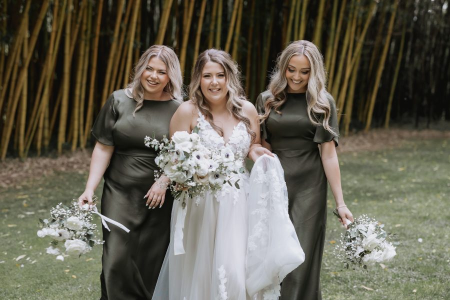 Happy Olive green bridesmaid walking with bride in front of the bamboo trees in olive green black walnut venue