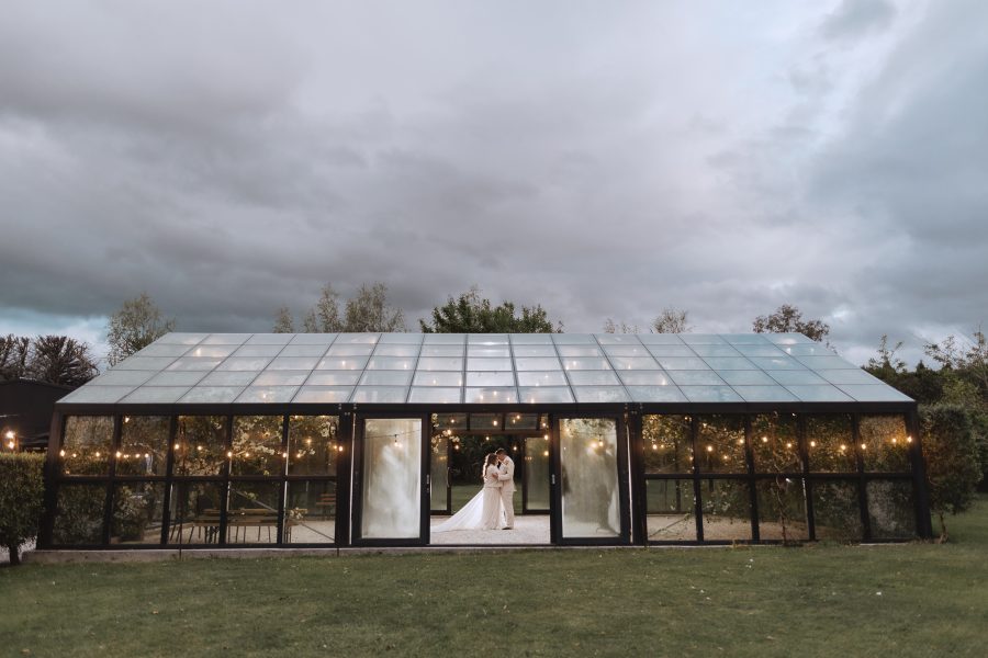 photo taken by Pure Images Photography of bride and groom inside glass house at Black Walnut wedding venue tauranga with clouds above