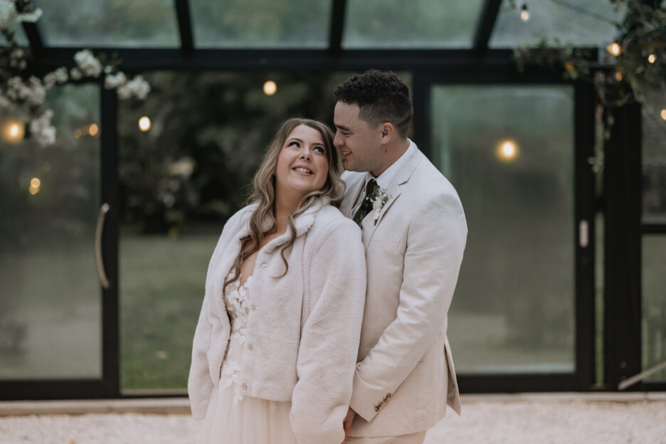 bride and groom snuggling in glass house at Black Walnut tauranga wedding venue