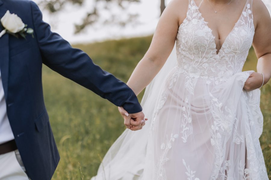 Wedding couple holding hands walking down hill in high grass