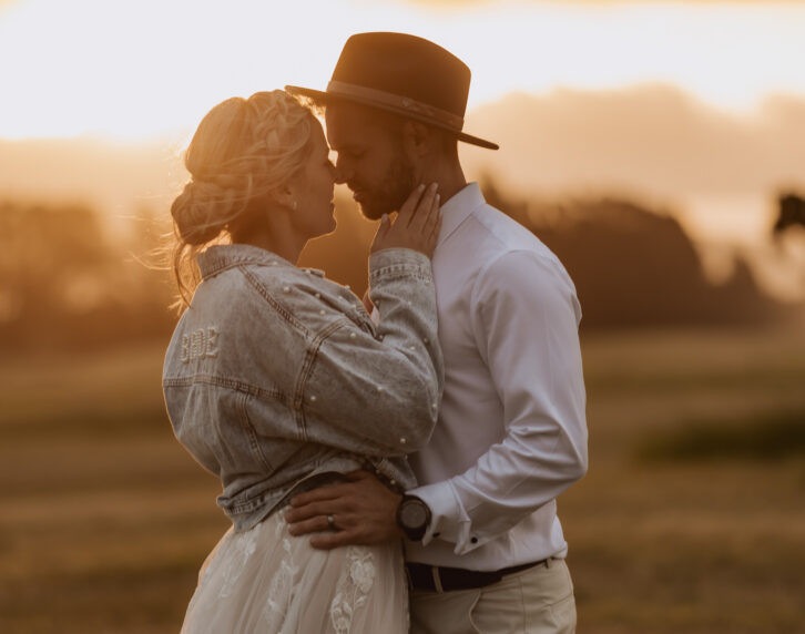 Bride holds grooms jaw line with denim jacket at golden hour