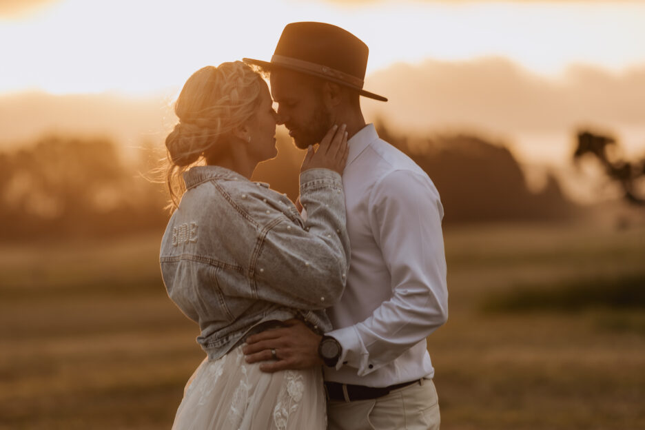 Bride holds grooms jaw line with denim jacket at golden hour