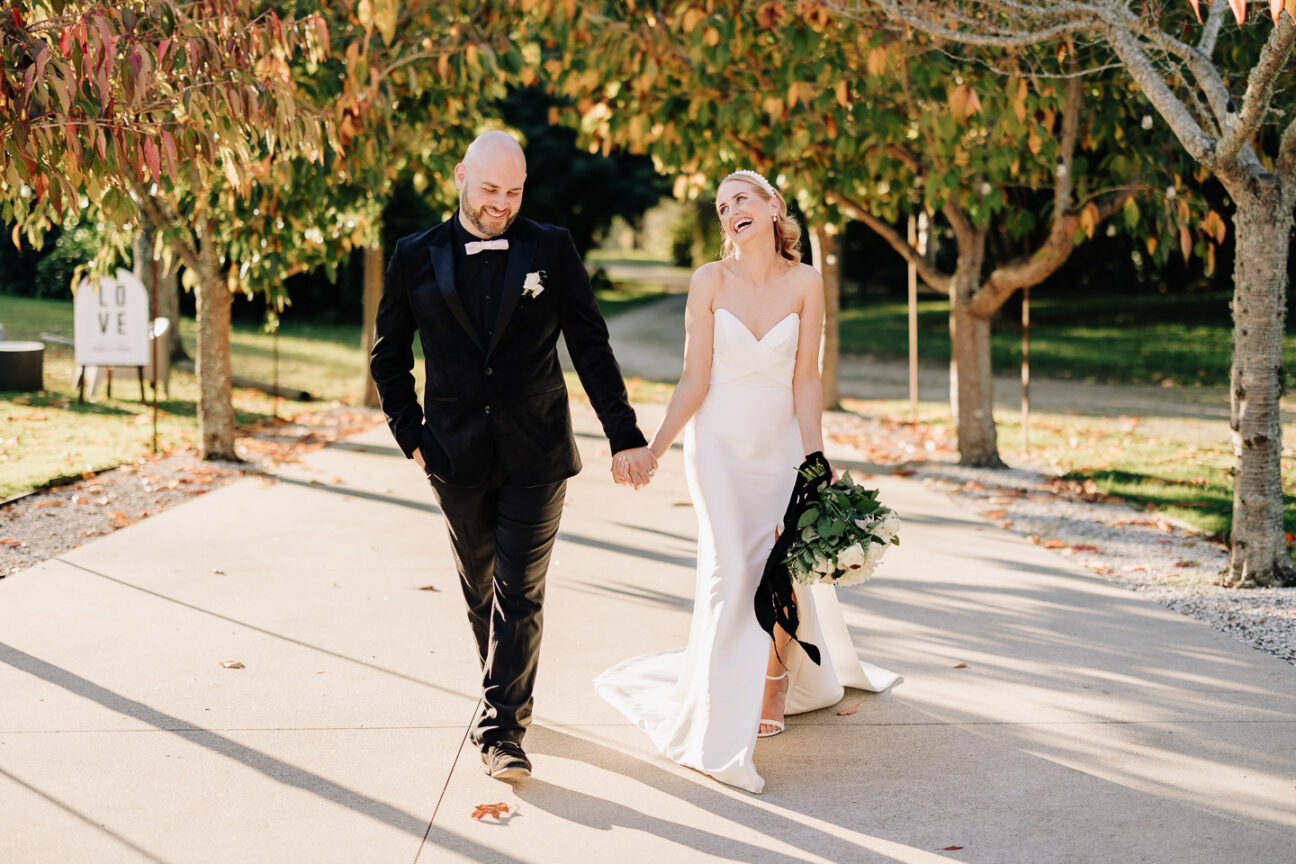 wedding photos as couple walk up driveway in between autumn trees