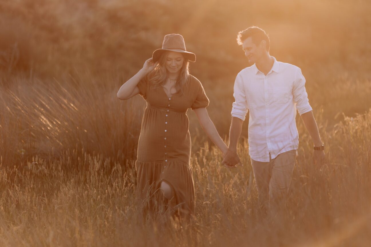 maternity photos of couple walking in sand dunes in golden light