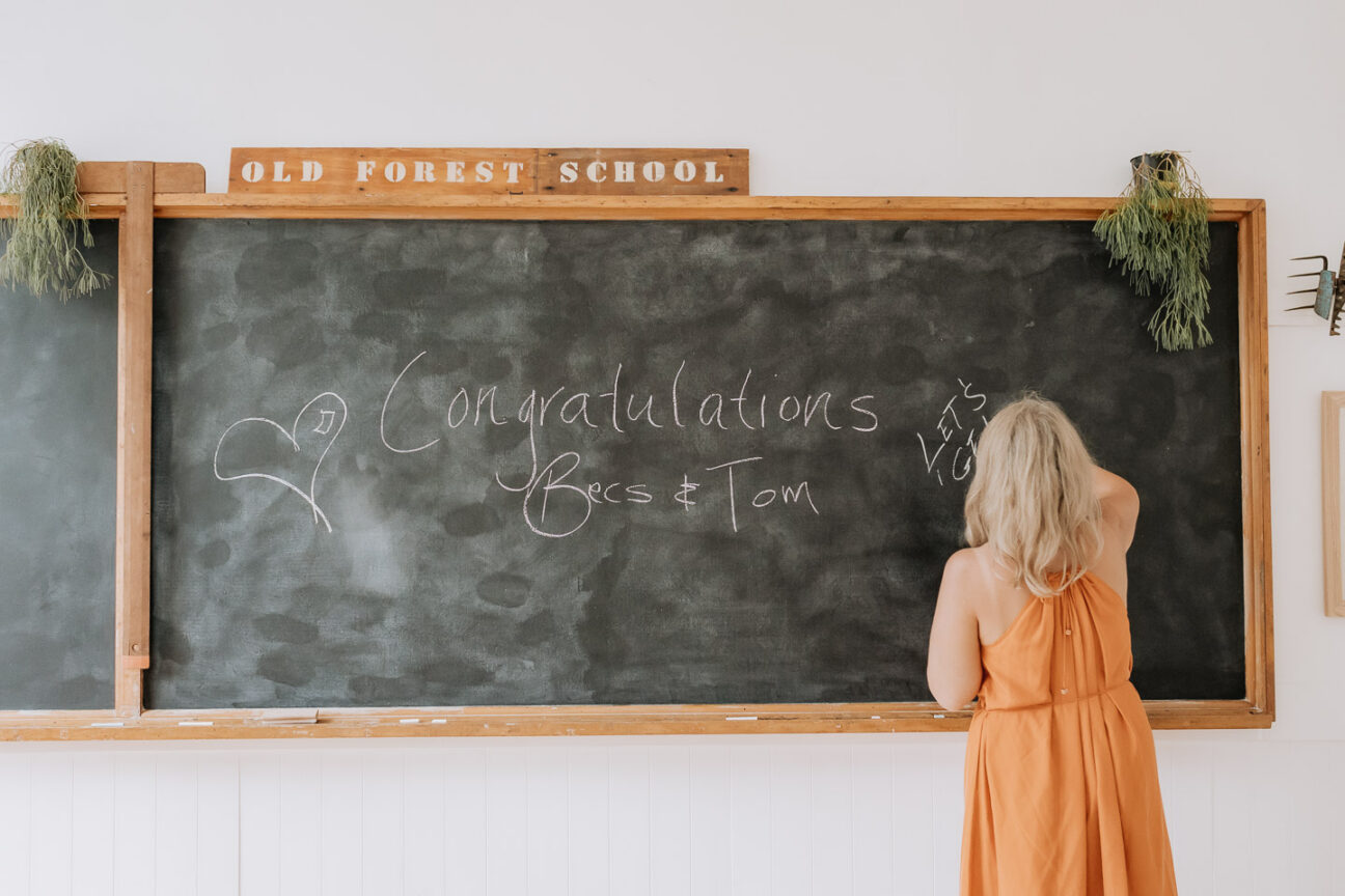 guest writes congratulations on black board in wedding school house