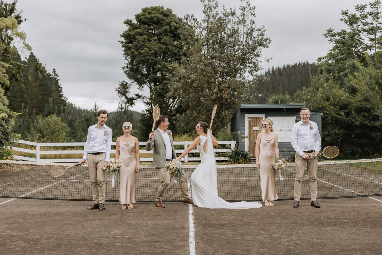 wedding party having fun on tennis courts holding rackets