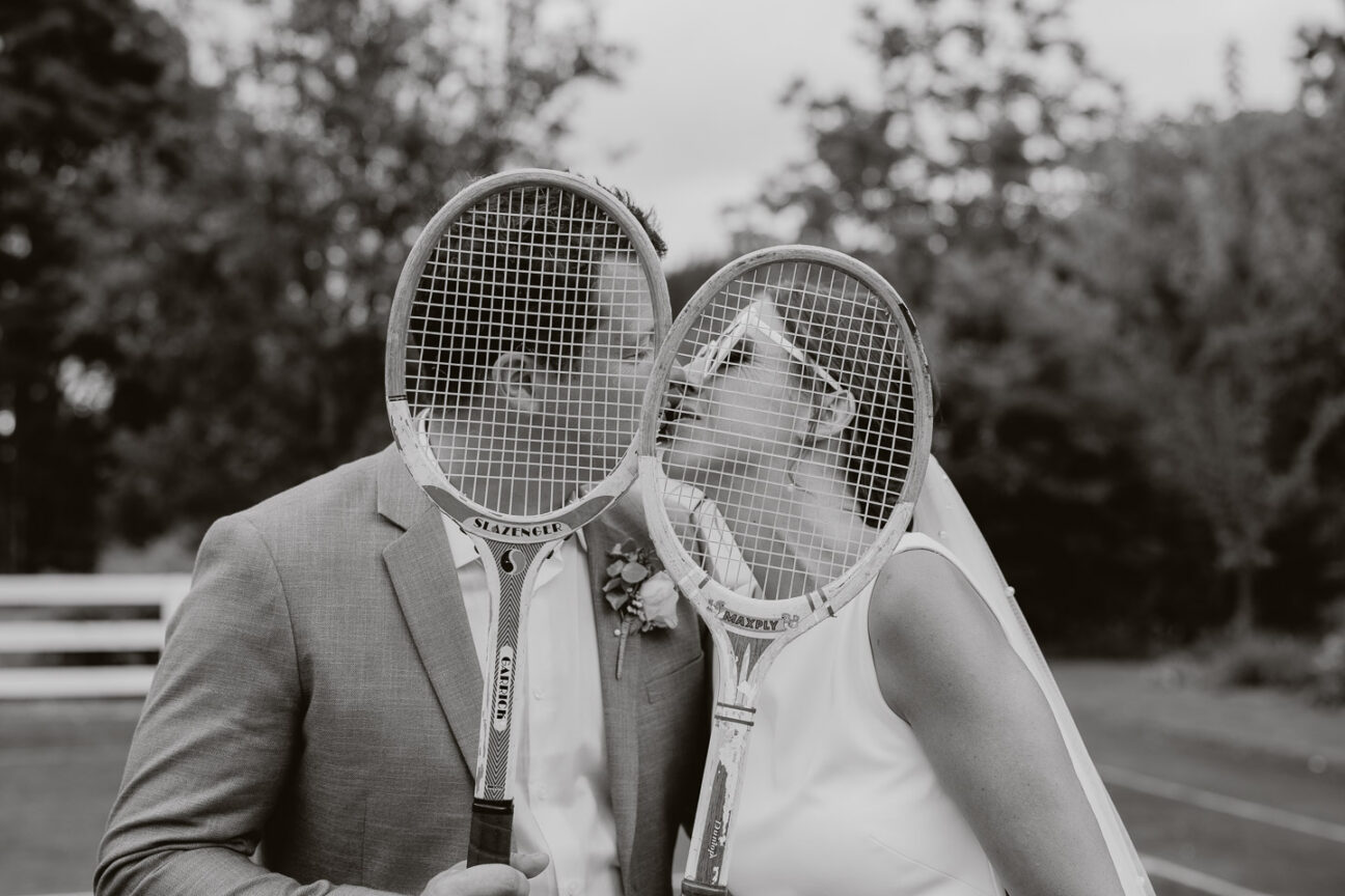 bride and groom kissing behind tennis rackets