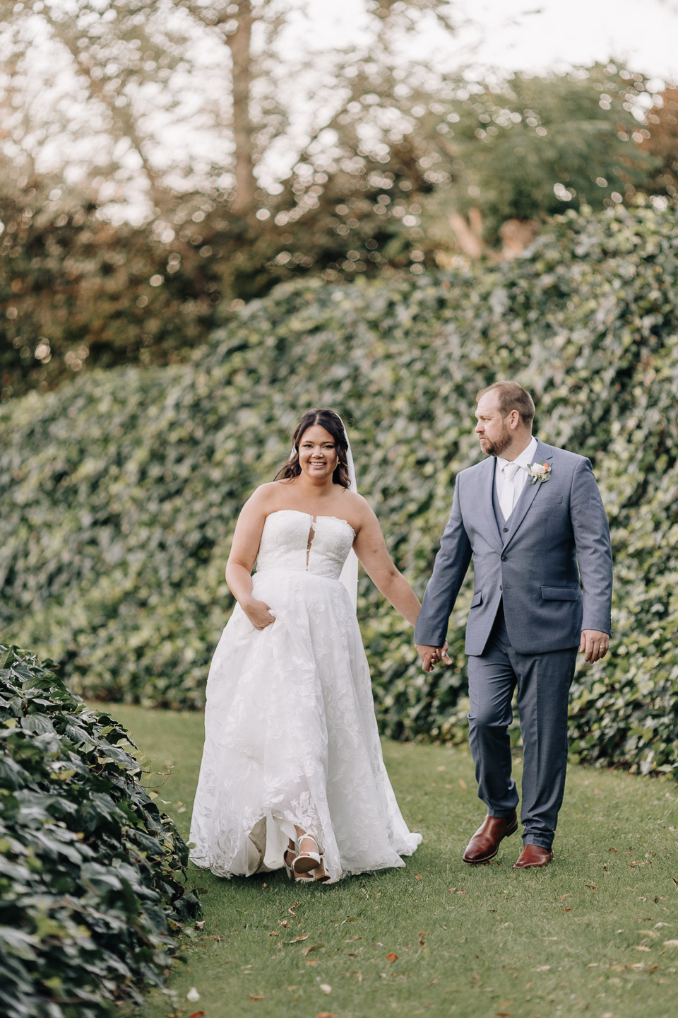 Bride and groom walking along ivy wall