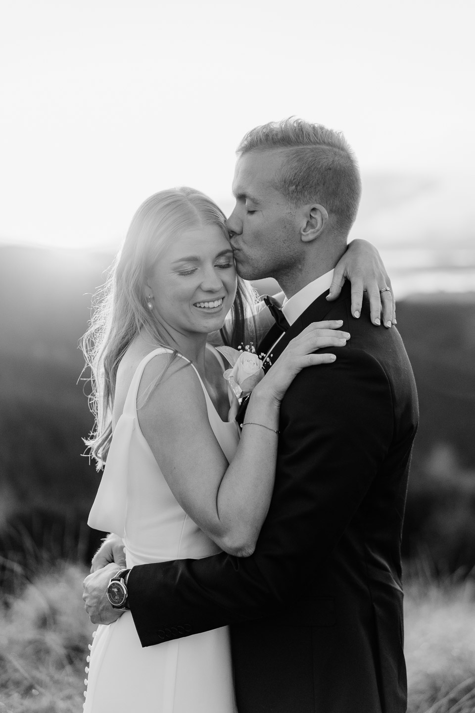 black and white wedding photography of a groom kissing his bride