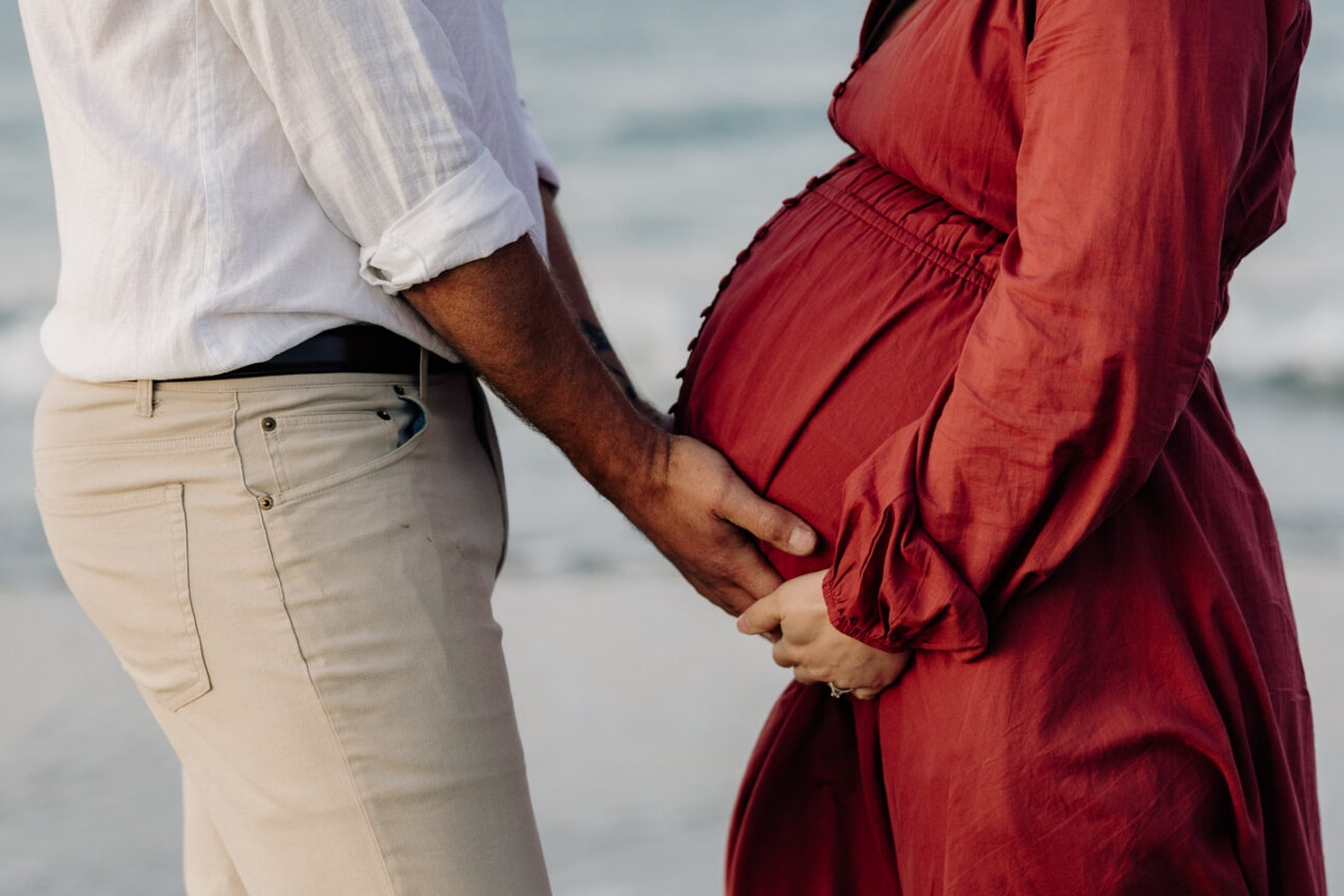 Hands hold pregnant belly for maternity shoot