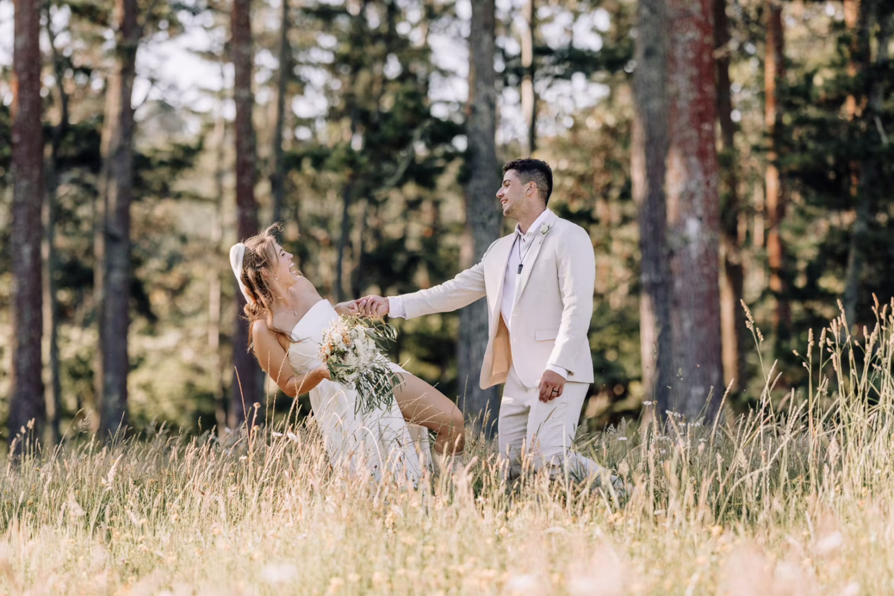 laughing bride and groom playing in a field of high grass by forest